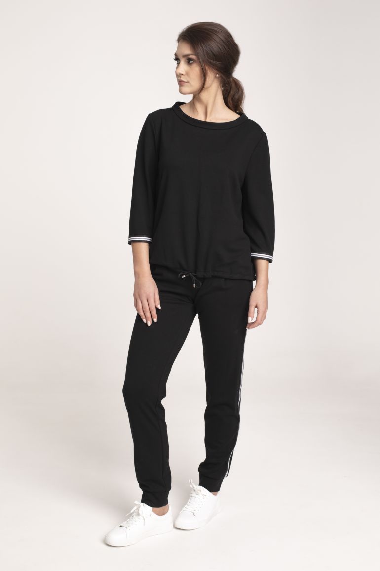 Modelka w czarnym dresie z lampasem Vito Vergelis. Czarna bluza ze stójką i taśmami i czarne spodnie Vito Vergelis.