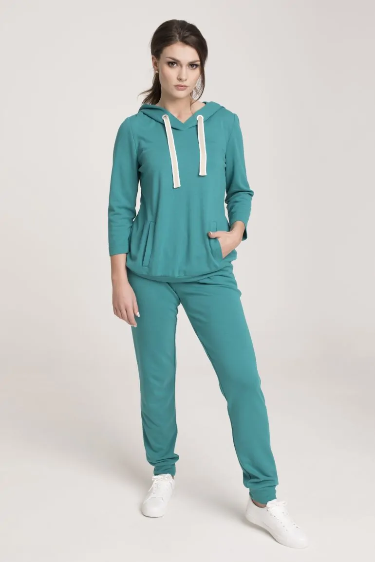 Modelka w zielonym dresie Vito Vergelis. zielona bluza z kapturem i kontrastowymi taśmami. Spodnie z lampasami.